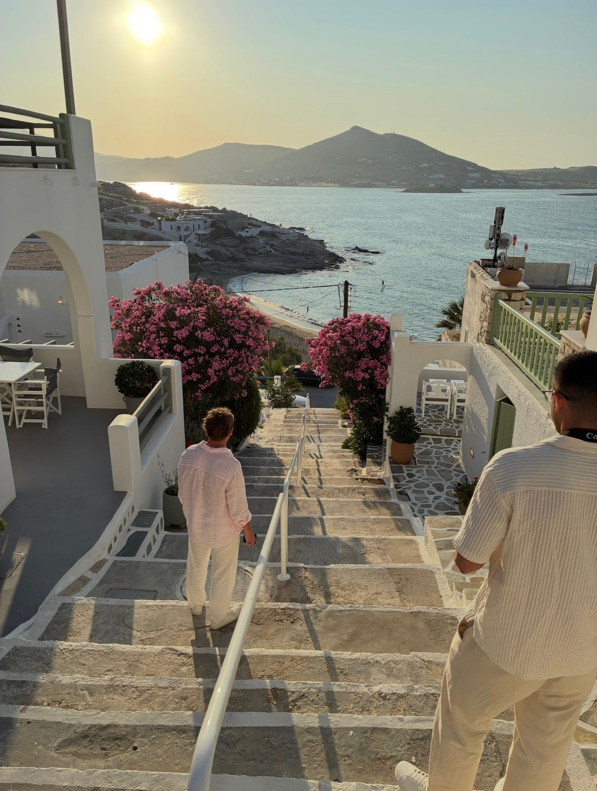 Two people walking up a stone staircase with a scenic view of the sea and mountains.